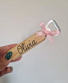 Een houten flesopener gepersonaliseerd met de naam Olivia en versierd met een roze strikje, handgemaakt door LOVI studio.