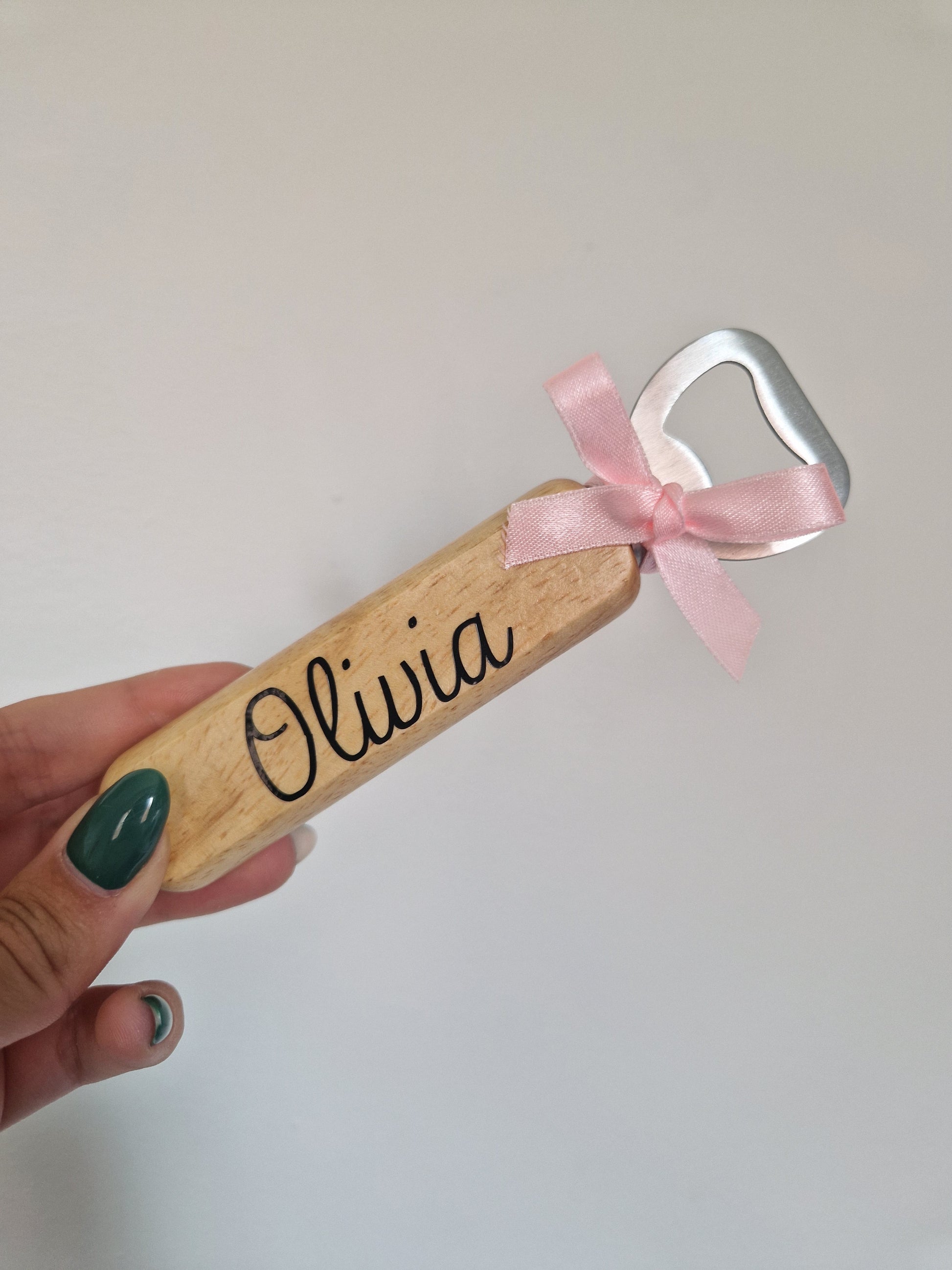 Een houten flesopener gepersonaliseerd met de naam Olivia en versierd met een roze strikje, handgemaakt door LOVI studio.