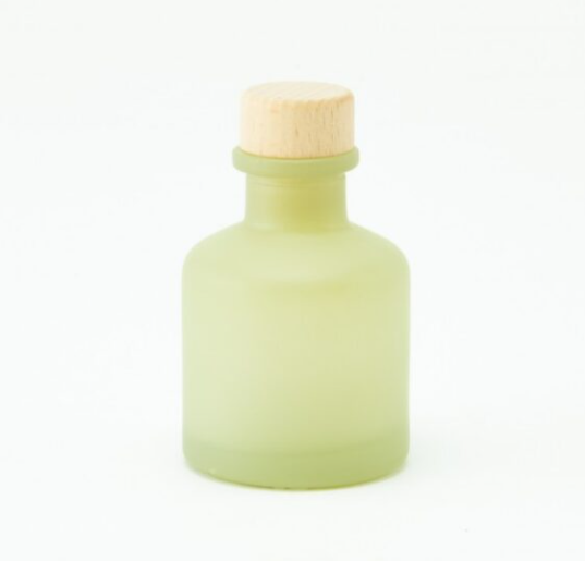 Minimalistisch matgroen glazen huisparfum flesje van 50ml met een houten dop tegen een witte achtergrond.