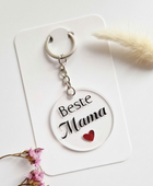 Transparante ronde acryl sleutelhanger met zwarte tekst 'Beste Mama' en een klein rood hartje, gepresenteerd op een witte kaart.