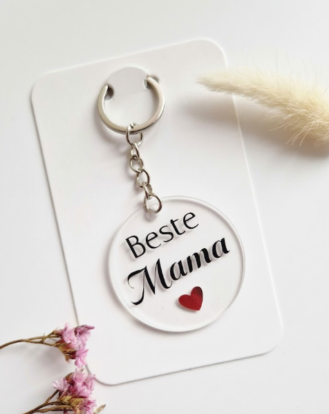 Transparante ronde acryl sleutelhanger met zwarte tekst 'Beste Mama' en een klein rood hartje, gepresenteerd op een witte kaart.