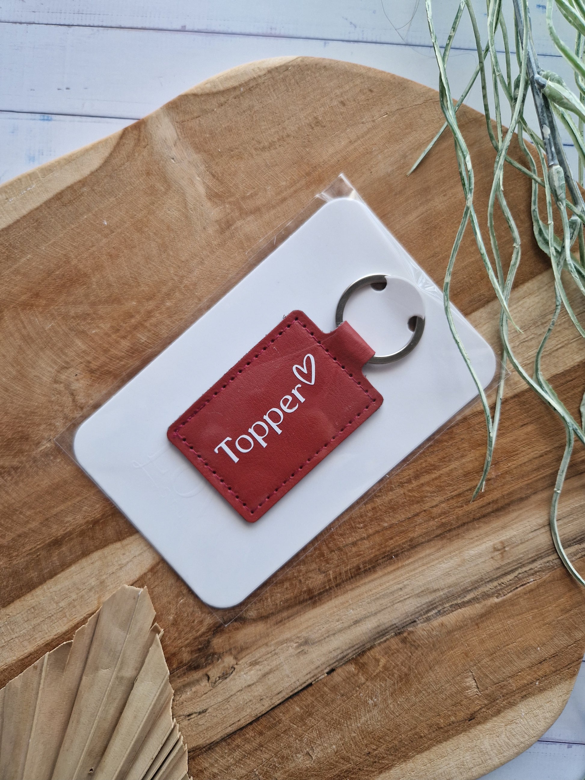 Rood lederen sleutelhanger met wit opschrift topper, ingepakt in een transparante verpakking