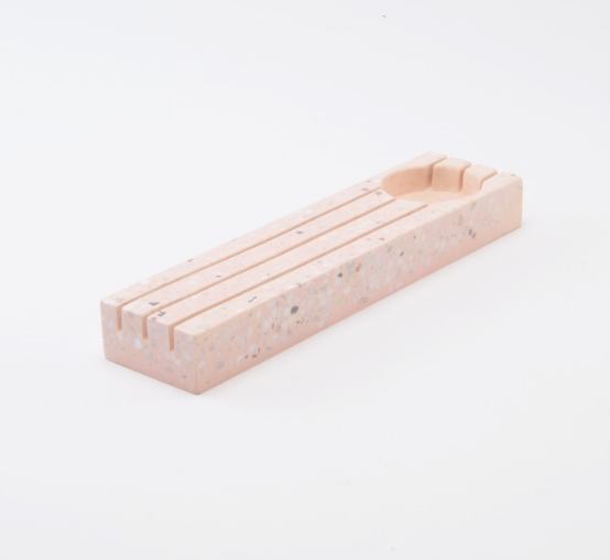 Rechthoekige roze terrazzo houder met gleuven voor kaarten of foto's en een rond uitgespaard bakje op een witte achtergrond.