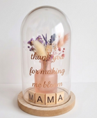 Glazen stolp met houten voet, gevuld met een roze vaasje met droogbloemen en houten letterblokjes die 'MAMA' spellen, met de gouden tekst 'thank you for making me bloom' op het glas tegen een witte achtergrond.